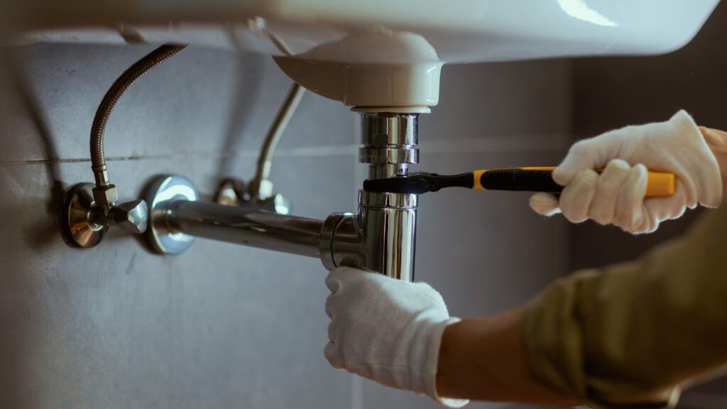 Gloved hands repairing pipework under a sink