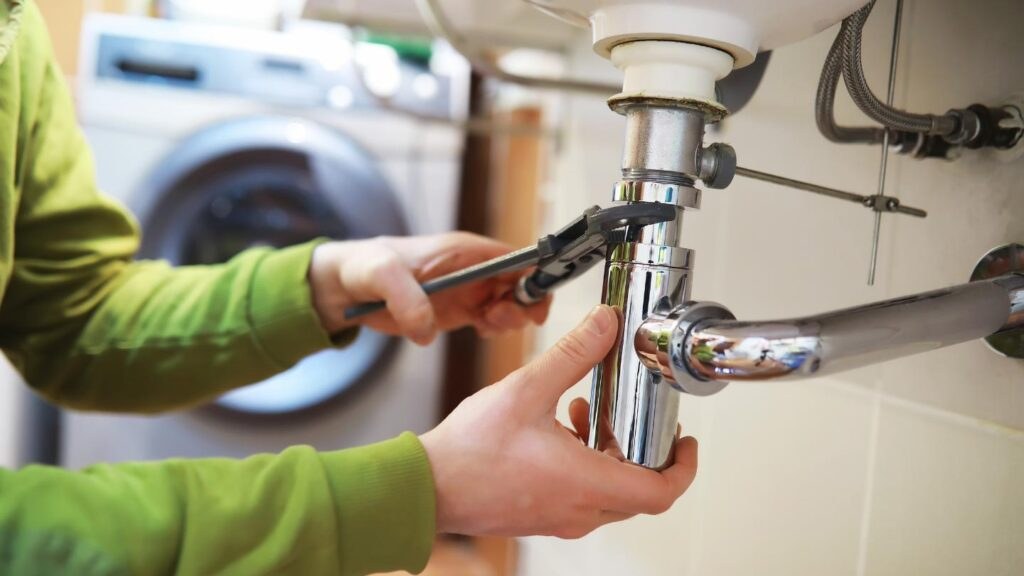 A plumber working under a kitchen sink during an emergency call